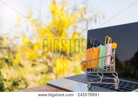 Mini Colourful Shopping Paper Bags In Trolley On Labtop Keyboard With Nature Background. Online Shop