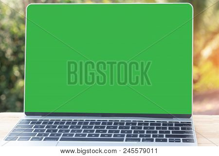 Mock Up Image Of Laptop With Blank Green Screen On Wooden Table Outdoor With Nature Background.