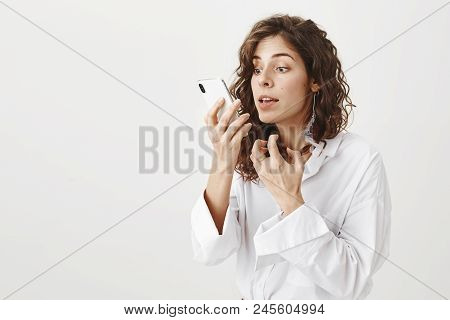 Portrait Of Annoyed Or Irritated Attractive Caucasian Woman With Feather Earring, Holding Smartphone