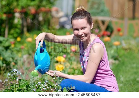 Smiling European Woman Watering Flowers With Water Can On A Croft.