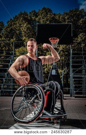 Strong Basketball Player In A Wheelchair Pose With A Ball On Open Gaming Ground.