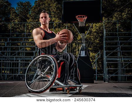 Cripple Basketball Player In A Wheelchair Holds A Ball On Open Gaming Ground.