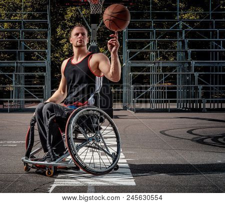 Disabled Basketball Player In Wheelchair Spinning Basketball On His Finger On Open Gaming Ground.
