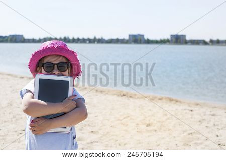Little Girl With A Tablet Computer In Hands. Good Summer Weekend On The Beach. Copy Spce