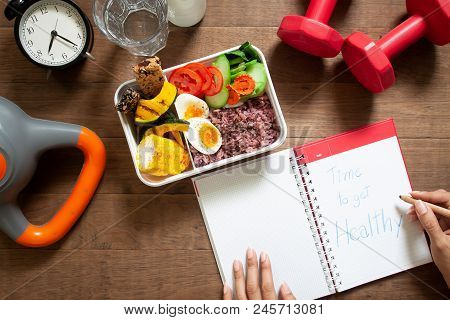 Healthy Concept With Nutrion Food In Lunch Box And Fitness Equipments With Woman Writing Time To Get