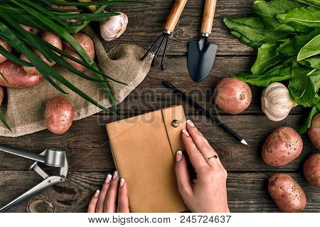 Notepad For Entries In Female Hands, Close-up. Top View On A Wooden Background With Garden Tools, Gr