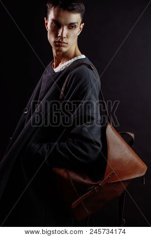Studio Shot Of A Handsome Young Male Model Wearing Dark Topcoat And Brown Lether Beg Over His Should