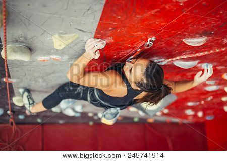 Beautiful Young Strong Woman Climbing On Rock Artificial Wall Top View. Female Climber Insured On Be