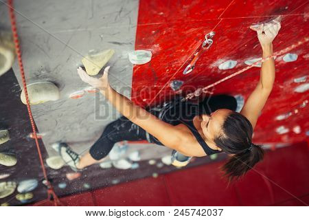 Beautiful Young Strong Woman Climbing On Rock Artificial Wall Top View. Female Climber Insured On Be