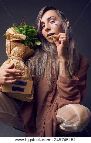 Stylish Woman In Biofuture Pompadour Style. Female In Fashion Cloths And The Green Plant In Paper Ba