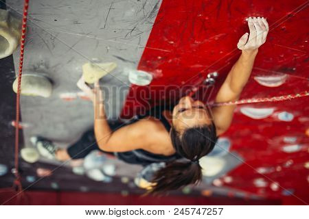 Beautiful Young Strong Woman Climbing On Rock Artificial Wall Top View. Female Climber Insured On Be