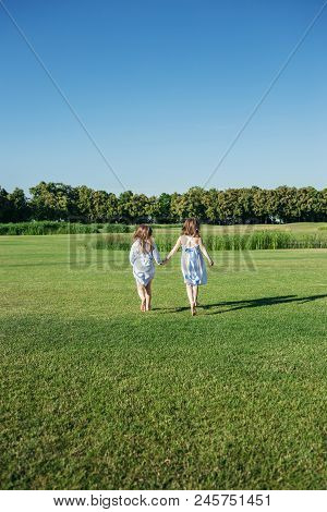 Two Girls Running Out On The Field. Sisters In Blue Dresses. Summer Leisure.
