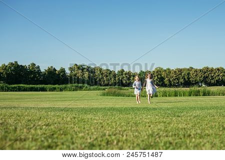 Two Girls Running Out On The Field. Sisters In Blue Dresses. Summer Leisure.