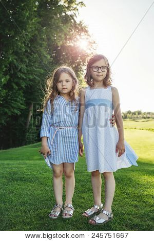 Two Attractive Girls Standing On The Field And Holding Hands. Sisters And Friends Love Concept.