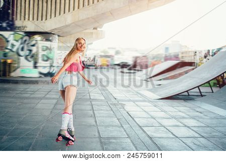 Blonde Girl Is Rollerblading. She Is Looking Back On Camera. Her Face Is Particulary Covered With He