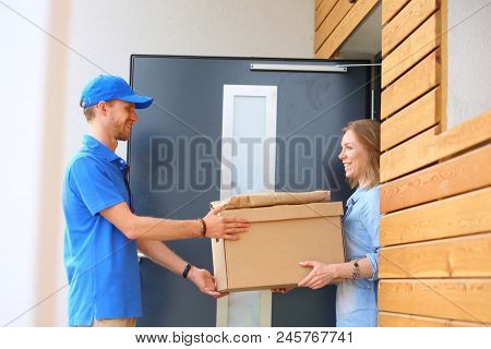 Smiling delivery man in blue uniform delivering parcel box to recipient - courier service concept. Smiling delivery man in blue uniform