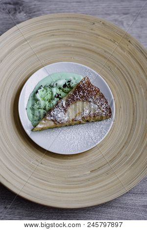 A Piece Of Apple Pie With Pistachio Ice Cream On A Background Of A Bamboo Plate In A White Plate.