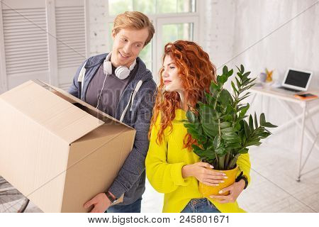 Own Place. Top View Of Positive Jovial Couple Holding Belongings And Flirting