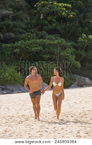 Happy Couple Laughing Together Holding Hands Running Having Fun Splashing Water In The Ocean Waves. 