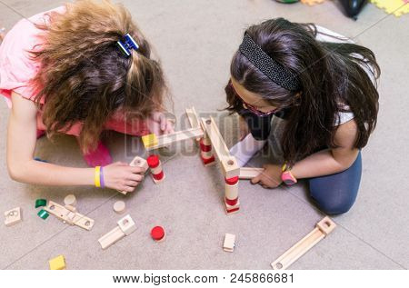 High-angle view of two pre-school girls sharing wooden toy blocks while building together a challenging structure on the floor at the kindergarten