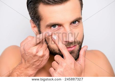 Close Up Portrait Of Young, Attarctive, Muscular Man Putting Contact Lenses In His Eye Over Gray Bac
