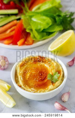 Hummus, Different Vegetables And Lettuce Leaves With Lemon And Garlic On A Light Background. Vegan F