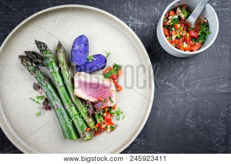 Modern fried tuna fish filet with green asparagus blue potatoes und vegetable chili relish as top view on a plate with copy space right