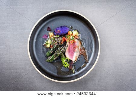 Modern fried tuna fish filet with green asparagus blue potatoes und vegetable chili relish as top view on a plate with copy space 