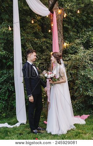Evening Summer Rustic Outdoor Wedding Ceremony. The Bride And Groom Holding Hands And See Each Other