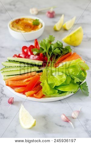 Hummus, Different Vegetables And Lettuce Leaves With Lemon And Garlic On A Light Background. Vegan F