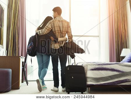 Full Length Of Loving Young Couple Looking Through Window In Hotel Room. Family On Honeymoon