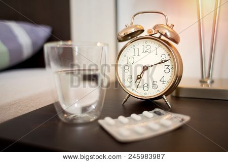 Closeup Of Alarm Clok, Water And Pills In Bedroom