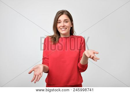Studio Portrait Of Attractive Caucasian Teenager In Red Pulover Shrugging Her Shoulders Having Some 