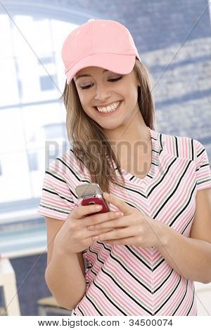 Casual meisje in roze Baseballcap met behulp van mobiele telefoon, glimlachend.
