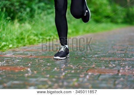 Legs Of Running Woman Atletic Spotsman Trains In The Summer Park. Outdoor Fitness Portrait After Rai