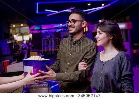Happy young affectionate couple buying popcorn and tickets in cinema while going to watch movie