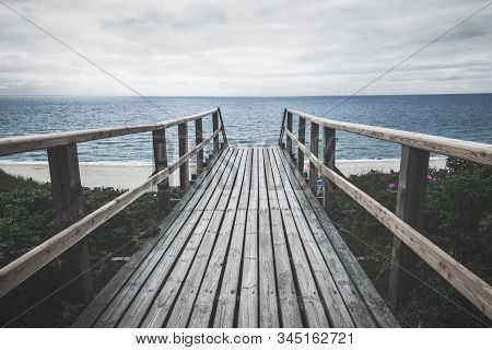 Wooden Bridge Over Roses Bushes Towards Beach And North Sea Water, On Sylt Island, Germany, On A Clo