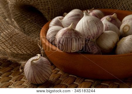Solo Garlic In Clay Plate On Straw Mat And Textile, View From Above