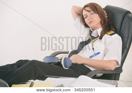 Overworked woman pilot wearing uniform with epaulettes resting or sleeping in briefing room
