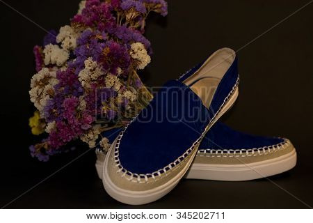 On Black Background, Pair Of Shoes, Blue Suede Slipons With White Thick Sole. Bouquet Of Dry Field F