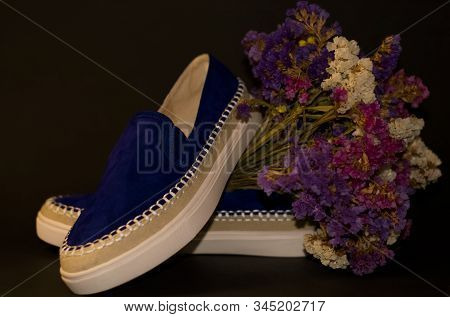 On Black Background, Pair Of Shoes, Blue Suede Slipons With White Thick Sole. Bouquet Of Dry Field F
