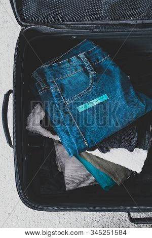 Travel Essentials For A Holiday, Luggage With Pile Of Clothes And Packing Everything Label On Them