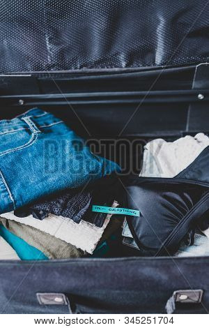 Travel Essentials For A Holiday, Luggage With Pile Of Clothes And Packing Everything Label On Them