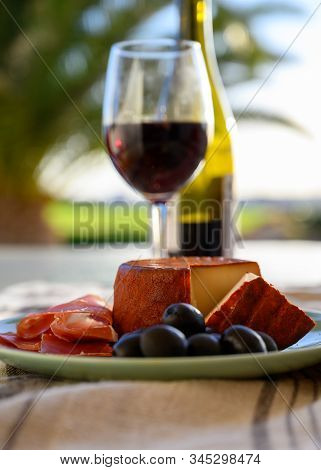 Tastes Of Spain, Jamon Iberian, Black Olives, Manchego Cheese With Red Paprika And Glass With Red Ri