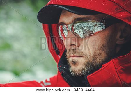 Caucasian Men In Red Rain Coat Hiking During Rainy Day. Expedition And Exploring Theme.