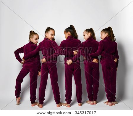 Group Of Young Smiling Girls Gymnasts In Dark Red Velvet Sport Costumes Standing Backwards And Embra