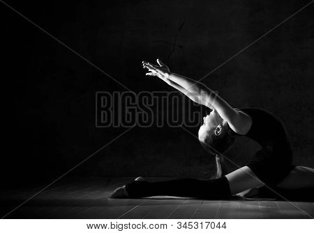 Young Girl Gymnast In Black Sport Body And Special Footwear Making Gymnastic Pose Over Dark Backgrou