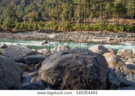 A Small Brooke Flowing Through The Valleys Of Himalayan Mountain With Big Rocks, Pebbles And Tall Pi