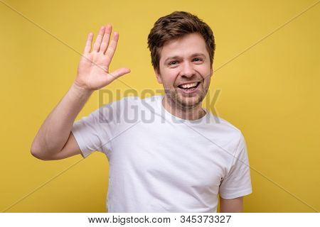 Young Man Dressed In White T-shirt Saying Hi Or Goodbye, Waving His Hand