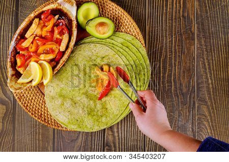 Woman Puts Fried Vegetables And Meat On Green Spinach Tortillas.